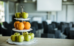 Ein Etagere mit Äpfeln und Orangen steht auf einem Tisch in einem Konferenzraum.
