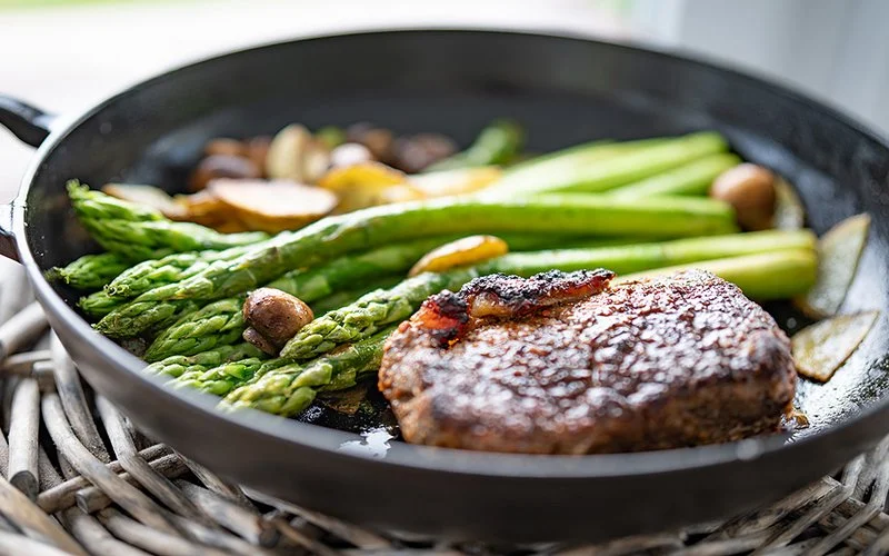 Gebratenes Rindesteak in einer Pfanne mit grünem Spargel.