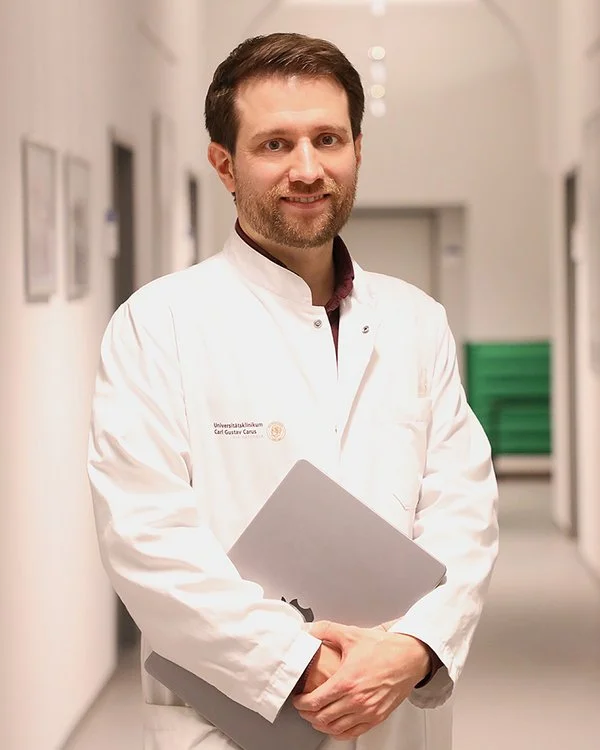 Prof. Dr. med. Jakob Nikolas Kather in weißem Arztkittel steht in einem Krankenhausflur und hält einen Laptop in den Händen.