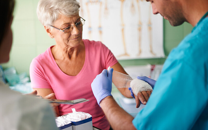 Eine Seniorin mit Wunde wird bei einem Arzt mit einem Verband versorgt.