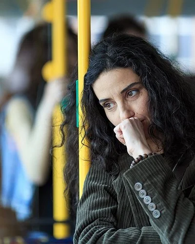 Eine junge Frau steht in einem Bus. Sie lehnt sich an eine gelbe Haltestange, dabei scheint sie intensiv zu grübeln.