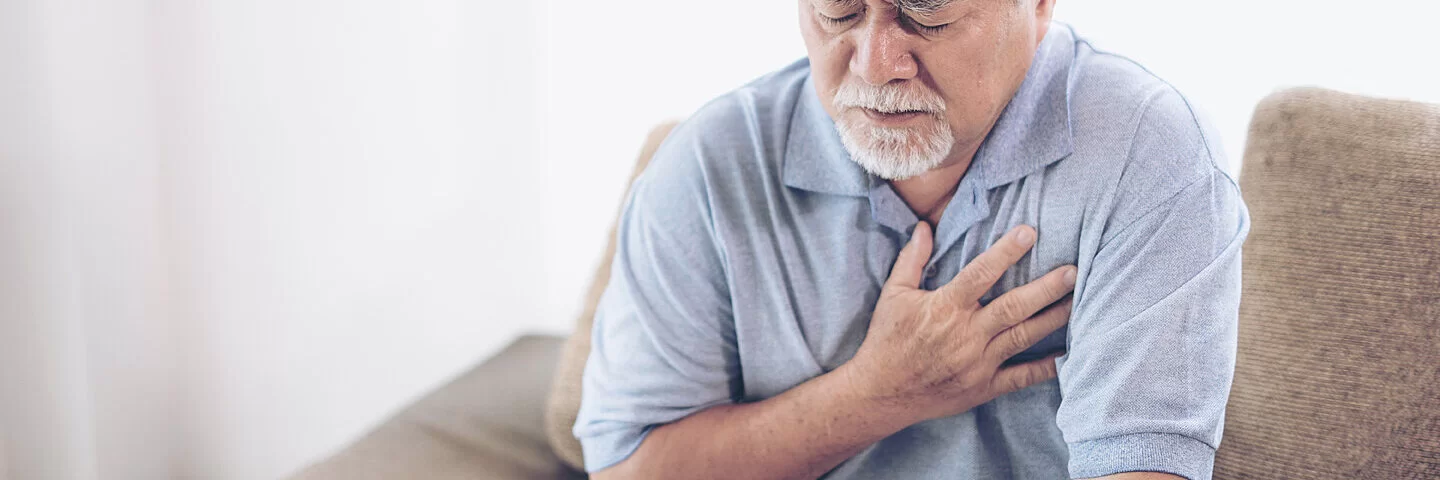 Ein älterer Mann fasst sich mit der Hand an den Brustkorb. Zu den typischen Beschwerden der koronaren Herzkrankheit gehört ein Engegefühl der Brust.