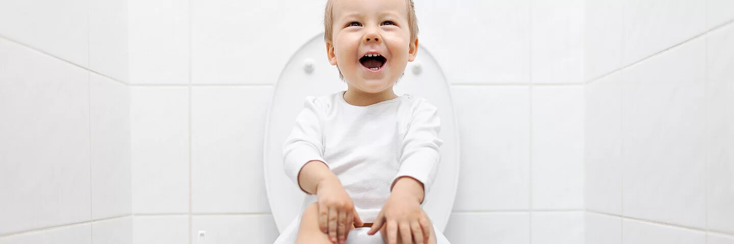 Ein fröhliches Kleinkind sitzt auf der Toilette.