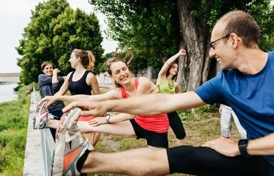 Mehrere Erwachsene dehnen sich gemeinsam im Freien beim Sport.