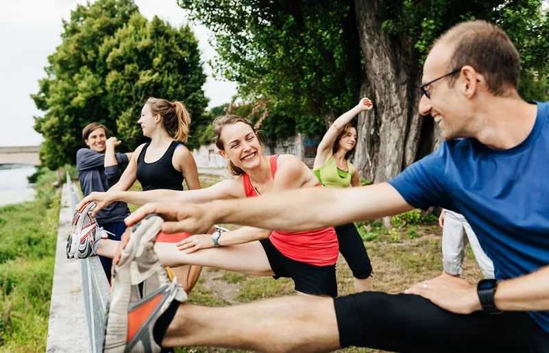 Mehrere Erwachsene dehnen sich gemeinsam im Freien beim Sport.