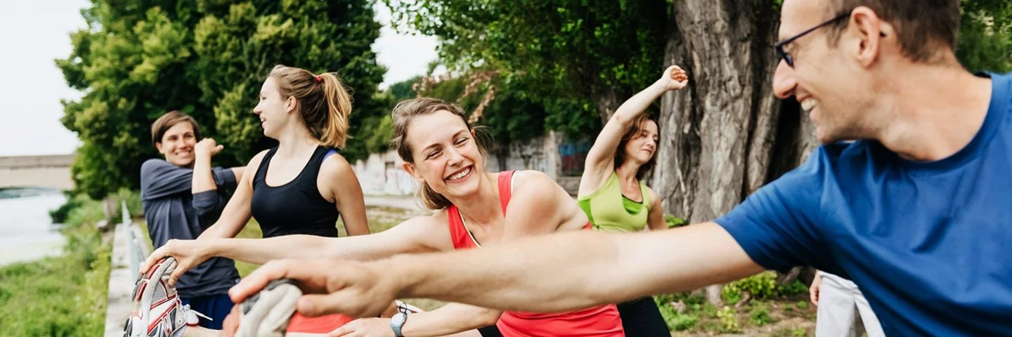 Mehrere Erwachsene dehnen sich gemeinsam im Freien beim Sport. 
