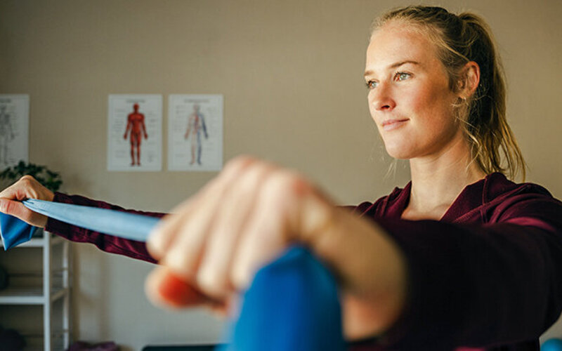 Eine jüngere Frau trainiert im Stehen mit einem Fitnessband.