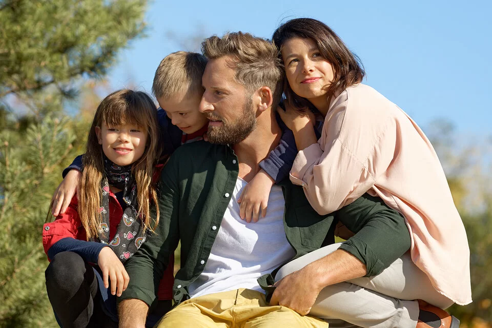 Ein Mädchen, ein Junge, Vater und Mutter posieren in der Sonne. In der AOK-Familienversicherung haben sie alle denselben Krankenversicherungsschutz.