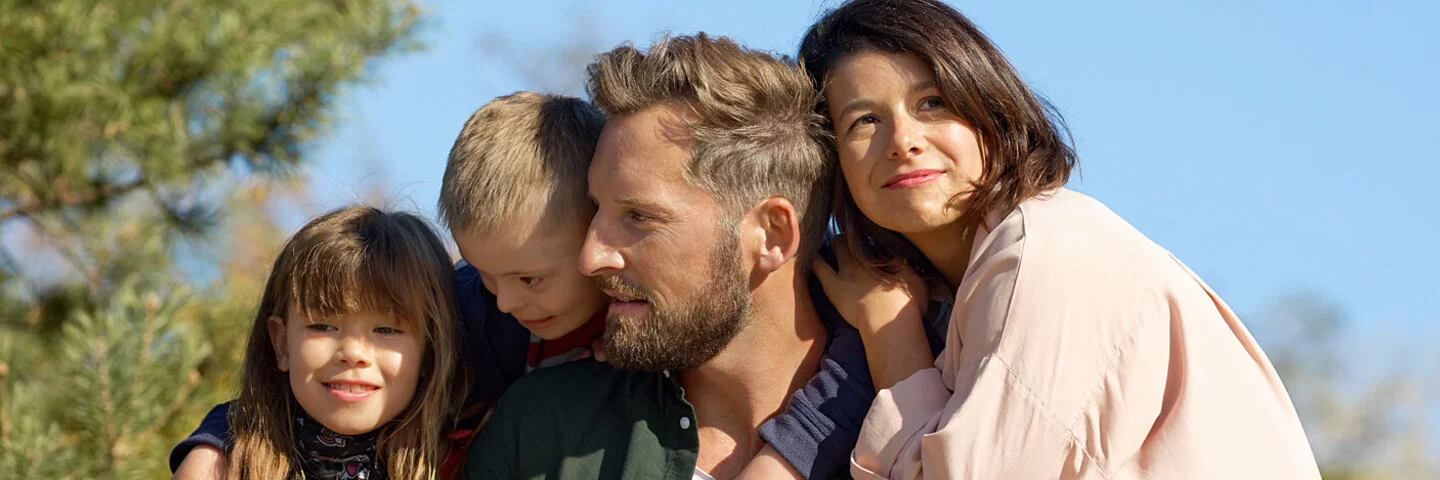 Ein Mädchen, ein Junge, Vater und Mutter posieren in der Sonne. In der AOK-Familienversicherung haben sie alle denselben Krankenversicherungsschutz.