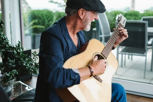 Ein älterer Herr probt bei sich zu Hause auf seiner Gitarre.