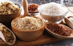 Viele verschiedene Reissorten eingefüllt in Schüsseln und Schippen stehen auf einem Holzbrett.