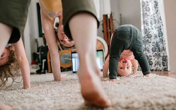 Eine Frau macht mit zwei Kindern eine Yoga-Übung im Wohnzimmer.