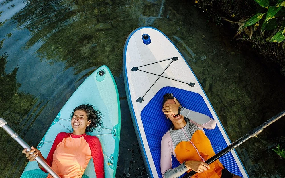 Zwei Personen liegen lachend mit dem Rücken auf ihren Stand-Up-Boards.