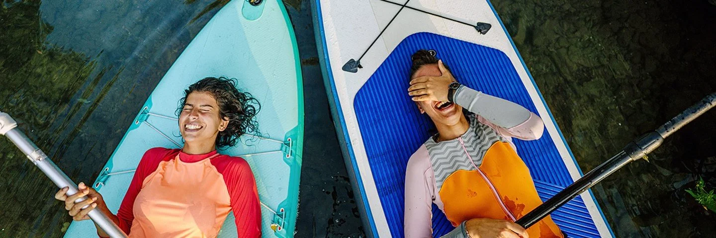 Zwei Personen liegen lachend mit dem Rücken auf ihren Stand-Up-Boards.