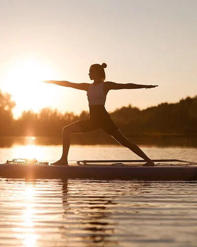 Frau macht SUP-Yoga im auf einem See im Sonnenuntergang.