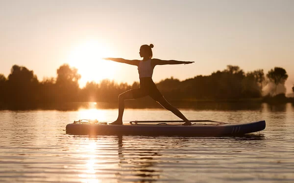 Frau macht SUP-Yoga im auf einem See im Sonnenuntergang.