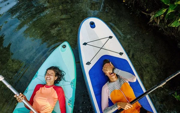 Zwei Personen liegen lachend mit dem Rücken auf ihren Stand-Up-Boards.
