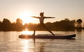 Frau macht SUP-Yoga im auf einem See im Sonnenuntergang.