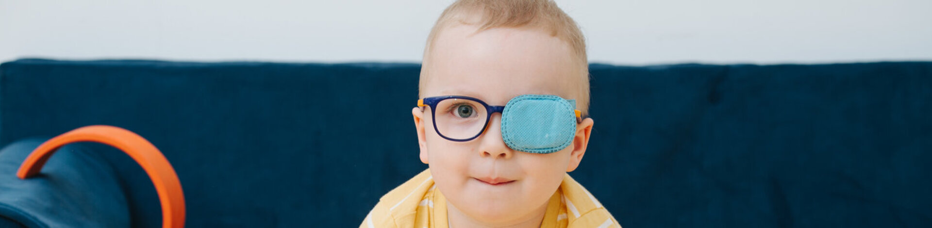 Ein Kleinkind trägt eine Brille, und ein Auge ist mit einem Pflaster zugeklebt. Amblyopie ist eine häufige Sehstörung bei Kindern. 