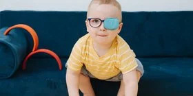 Ein Kleinkind trägt eine Brille, und ein Auge ist mit einem Pflaster zugeklebt. Amblyopie ist eine häufige Sehstörung bei Kindern.