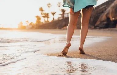 Eine Frau geht in Badekleidung barfuß an einem tropischen Sandstrand spazieren.