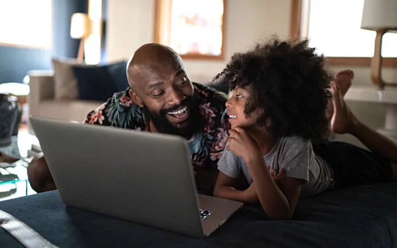 Vater schaut mit seiner Tochter auf einen Laptop.