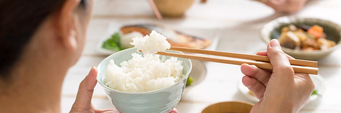 Resteverwertung von Reis: Eine Frau sitzt am Küchentisch und isst den Reis vom Vortag.
