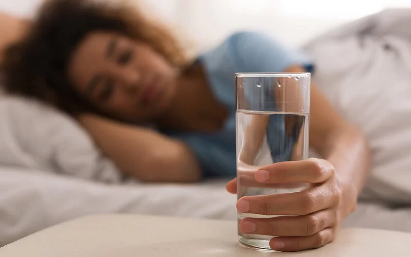 Frau, die unter regelmäßigen Synkopen leidet, trinkt vor dem Aufstehen ein Glas Wasser.