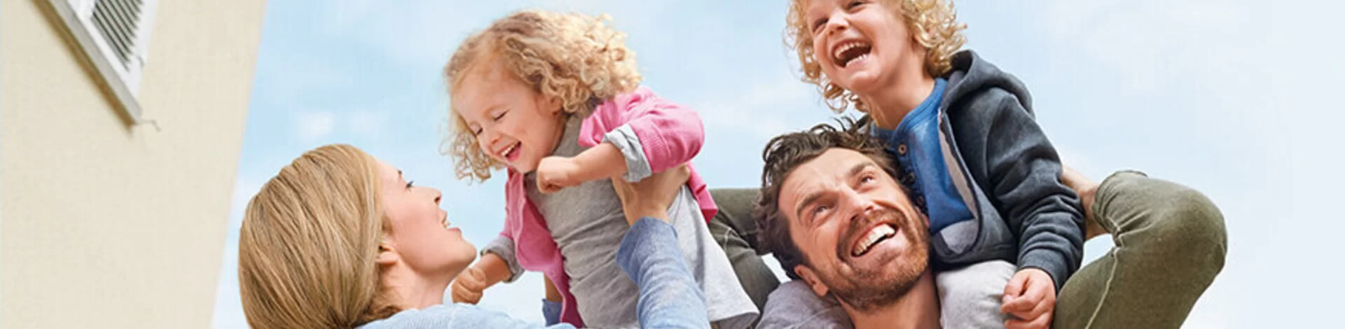Eine Familie beim Spielen. Der Vater trägt seinen Sohn auf dem Rücken. Die Mutter hebt ihre Tochter hoch.