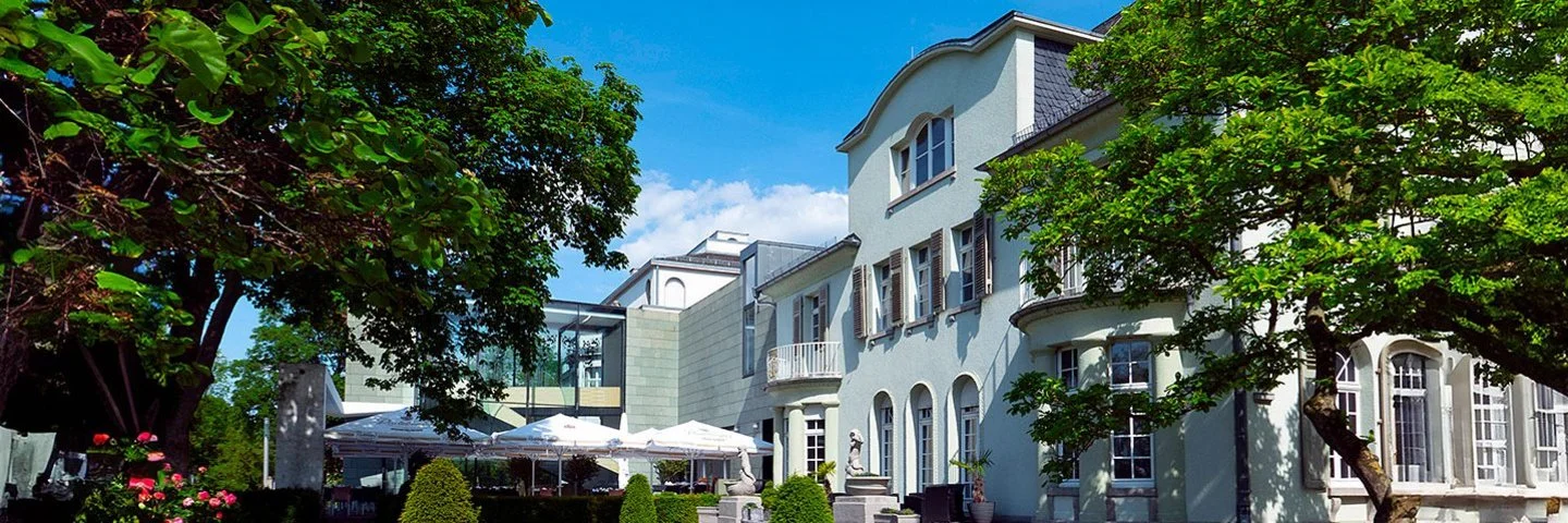 Opelvilla in Rüsselsheim mit grünem Garten bei blauem Himmel.