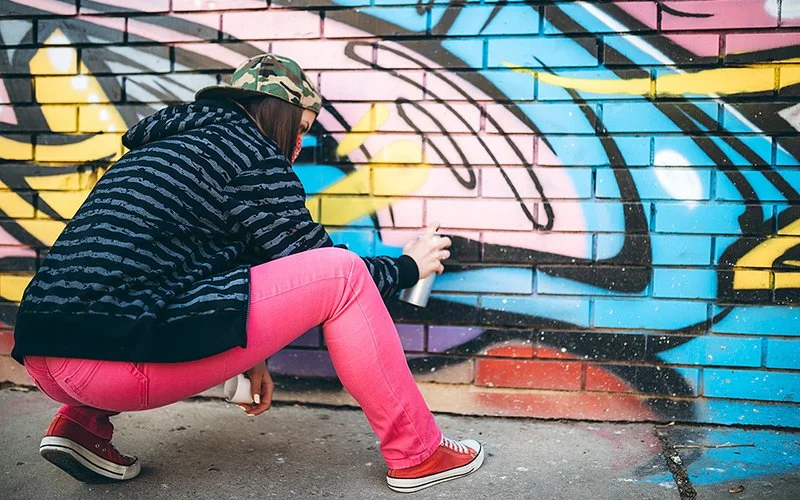 Eine junge Frau sprüht Graffiti an eine Wand.