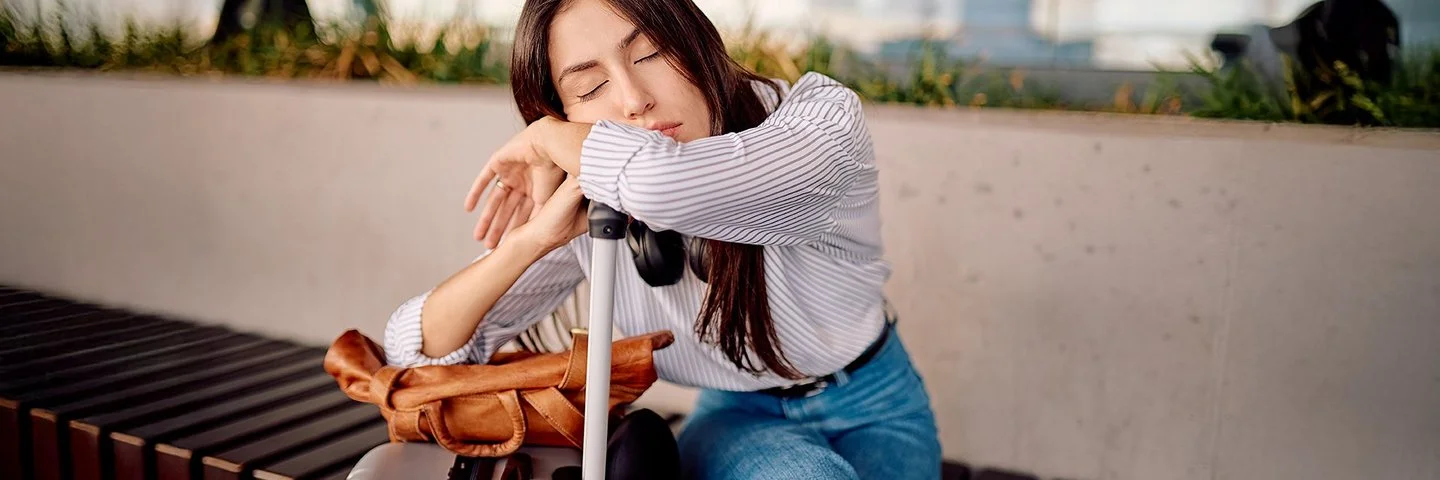 Eine junge Frau schläft erschöpft auf ihrem Gepäck im Flughafen.