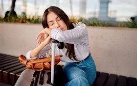 Eine junge Frau schläft erschöpft auf ihrem Gepäck im Flughafen.