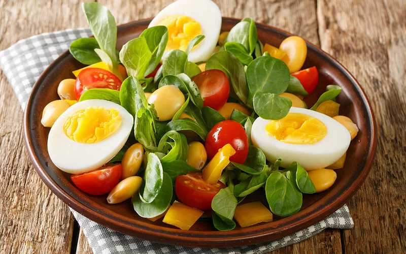 Ein Teller Feldsalat mit Lupinenbohnen, gekochten Eiern, Kirschtomaten und gelber Paprika.