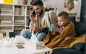 Vater und Sohn haben einen Atemwegsinfekt und ruhen sich gemeinsam auf dem Sofa aus.