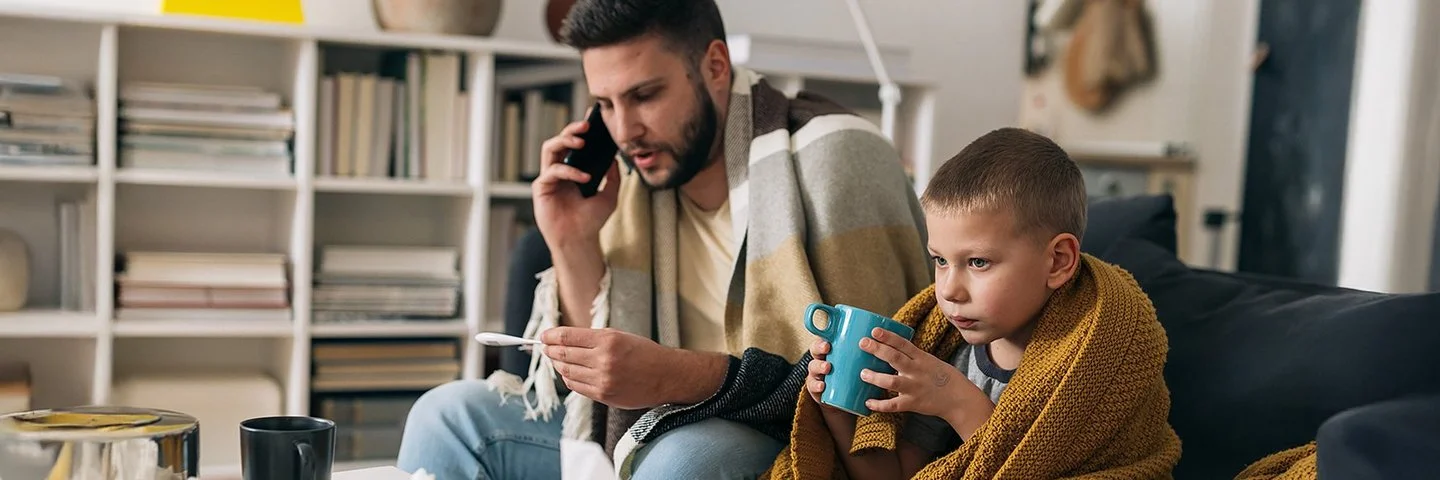 Vater und Sohn haben einen Atemwegsinfekt und ruhen sich gemeinsam auf dem Sofa aus.