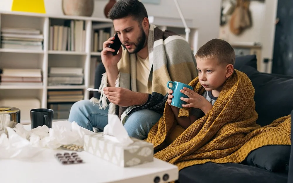 Vater und Sohn haben einen Atemwegsinfekt und ruhen sich gemeinsam auf dem Sofa aus.