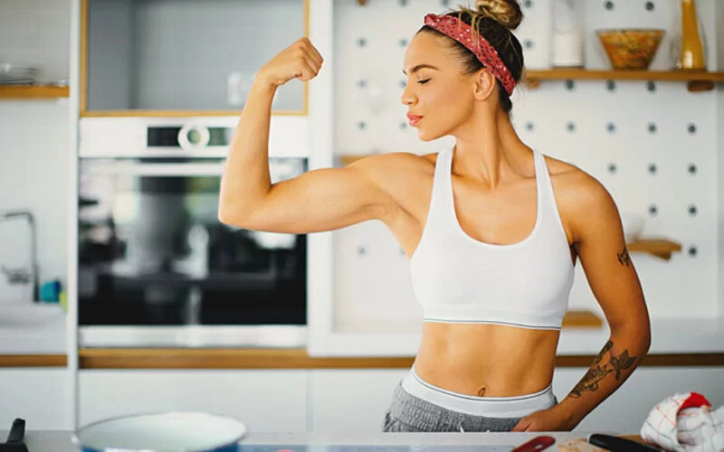 Eine Frau bereitet sich eine proteinreiche Mahlzeit zum Muskelaufbau zu und spannt die Muskeln an.