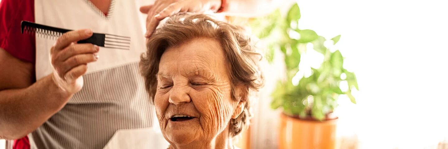 Altenpflegerin kämmt einer alten Frau behutsam die Haare.