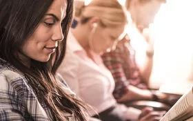 Eine Frau sitzt neben zwei Mitreisenden im Flugzeug und liest ein Buch