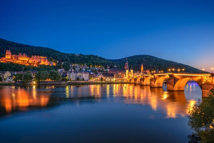 Der Neckar und das beleuchtete Panorama Heidelbergs bei Nacht.