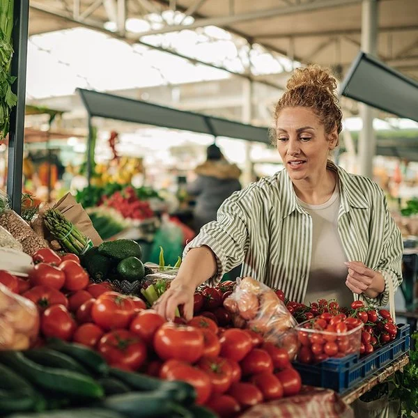Eine Frau kauft Gemüse an einem Marktstand. Sie greift prüfend nach den Tomaten.