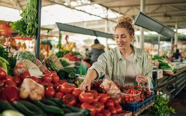 Eine Frau kauft Gemüse an einem Marktstand. Sie greift prüfend nach den Tomaten.