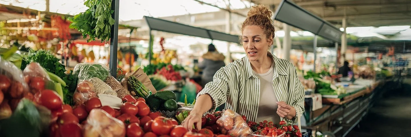 Eine Frau kauft Gemüse an einem Marktstand. Sie greift prüfend nach den Tomaten.