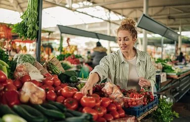 Eine Frau kauft Gemüse an einem Marktstand. Sie greift prüfend nach den Tomaten.
