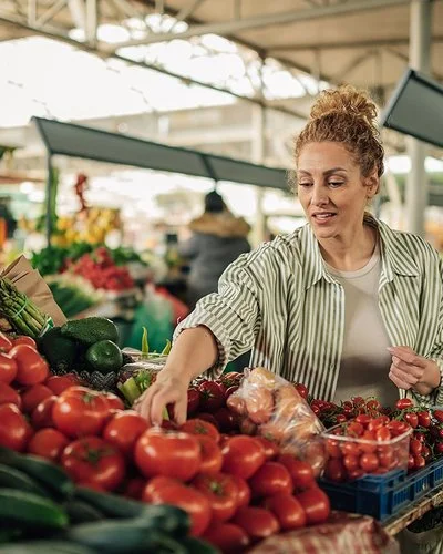 Eine Frau kauft Gemüse an einem Marktstand. Sie greift prüfend nach den Tomaten.