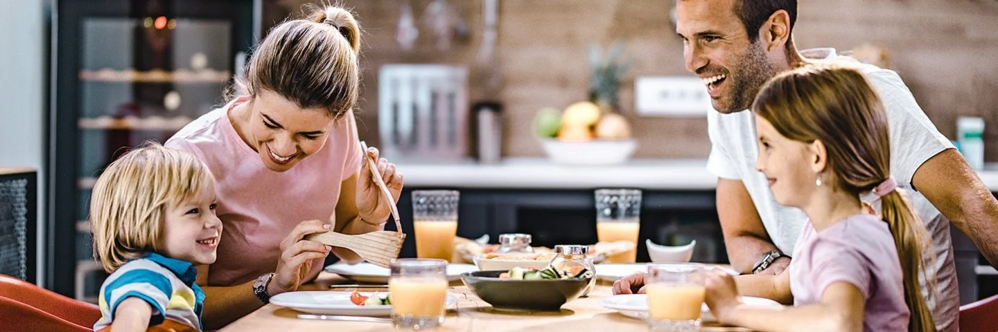 Eltern mit zwei Kindern unterhalten sich fröhlich beim Abendessen in der Küche.
