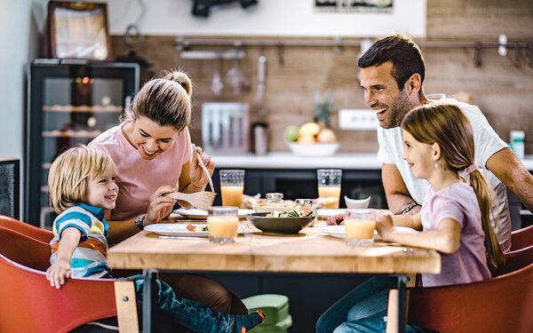 Eltern mit zwei Kindern unterhalten sich fröhlich beim Abendessen in der Küche.