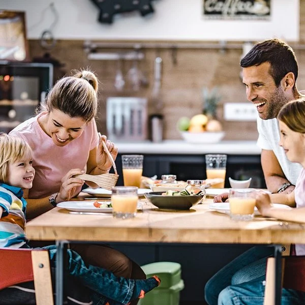 Eltern mit zwei Kindern unterhalten sich fröhlich beim Abendessen in der Küche.