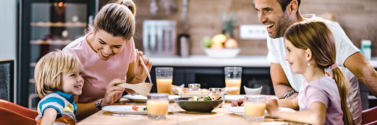 Eltern mit zwei Kindern unterhalten sich fröhlich beim Abendessen in der Küche.